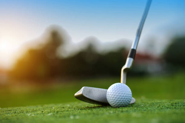 Golf clubs and golf balls on a green lawn in a beautiful golf course with morning sunshine. The ball at the hole on the golf course.